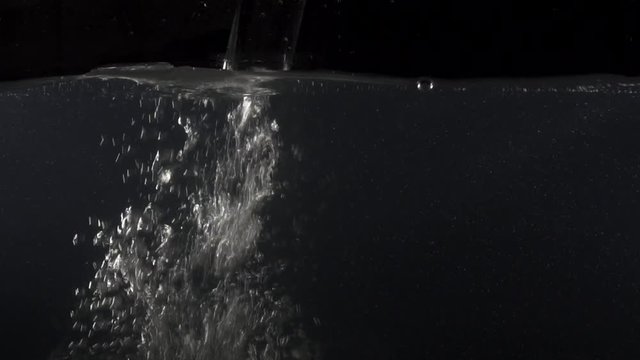 Closeup of pouring water into water on the black background