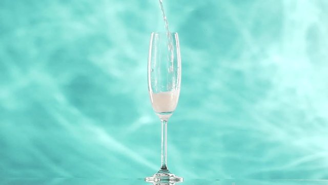 Cream-primrose coloured soda water pouring into champagne flute glass standing on cyan smoky background in slowmotion