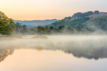 Fototapeta na wymiar Misty spring morning at Rydal Water in the English Lake District with calm reflections in water.