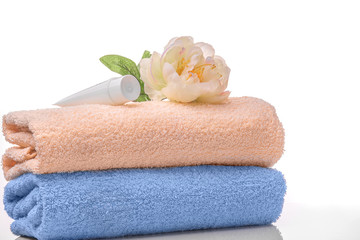 Obraz na płótnie Canvas Two Terry towels, white tube and peony flower on a white background. Blue and cream towels are already on the stack. Studio photography. High key. The concept of purity freshness SPA
