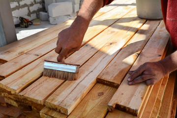 Construction worker is working with wooden beam. The worker brushes the preservative liquid on the folded boards and boards.