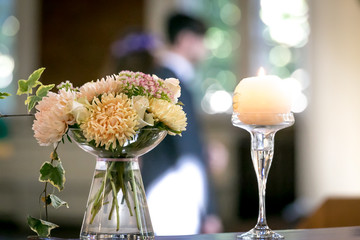 Multiple colored flower in glass vase beside of a lit candle.