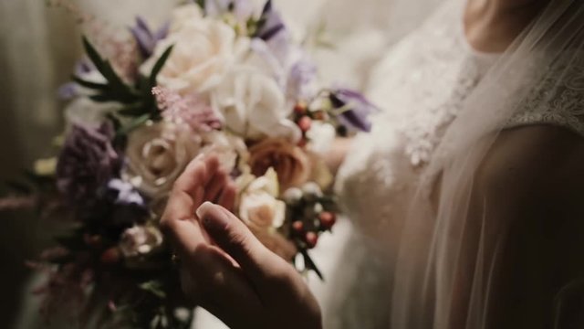 Close-up view of young bright with wedding bouquet. Woman looks and touches the natural flowers composition.