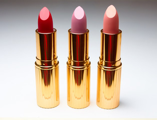Three open lipsticks of red, pink and beige colors on a white background.