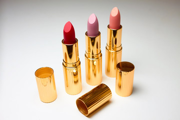 Three open lipsticks of red, pink and beige colors on a white background. Near open caps from lipsticks