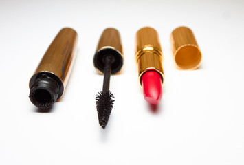 Red open lipstick and black mascara lie on a white background. Horizontal frame. Cosmetics in luxurious gold packaging. Fashionable screensaver