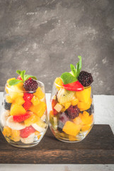 Vegan dietary foods. Vitamins. Dessert. Summer. Salad of fresh organic fruits - mango, peach, apple, banana, kiwi, strawberry, blackberries. In glasses. On a white concrete table. copy space