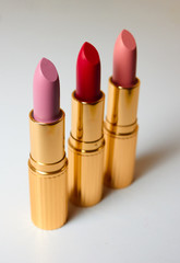 Three matte lipsticks in luxurious gold tubes stand on a white surface. Vertical photo. Red lipstick, pink and lipstick flesh-colored