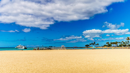 The beautiful sand of Waikiki beach under blue and partly cloudy sky makes it one of the world's most famous beaches. Located in Honolulu on the Hawaiian island of Oahu