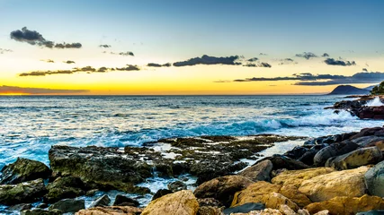 Fototapeten Sunset over the horizon with a few clouds and waves crashing on the rocky shores of the west coast of the tropical Hawaiian island of Oahu © hpbfotos