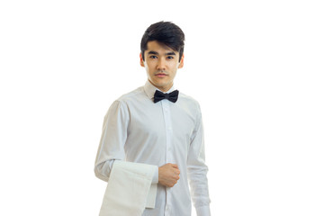 beautiful strong young waiter in a white shirt with a butterfly looks straight and keeps towel on hand