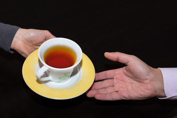 A hand that offers a cup of tea and the other one that receives it