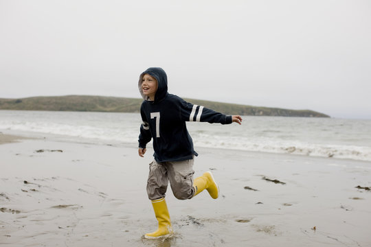 Boy on the beach wearing rubber boots.
