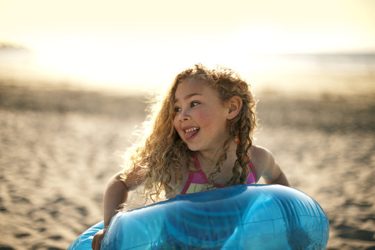 Young girl playing with an inflatable ring on the sand at the beach.