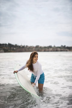 Young woman heading into the surf with a surfboard.