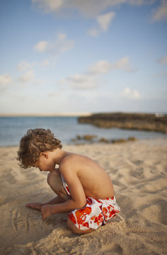 Young boy drawing a tic tac toe grid in the sand on a beach.