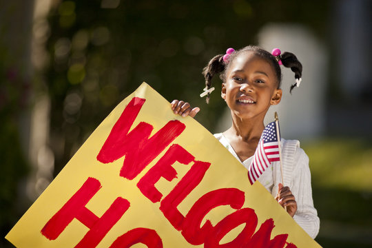 Young girl holding an American flag and a welcome home sign.