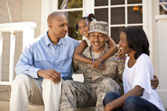 Portrait of a smiling young soldier sitting with his family outside his home.