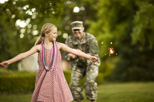 Young girl dancing with sparklers in the back yard with her father.