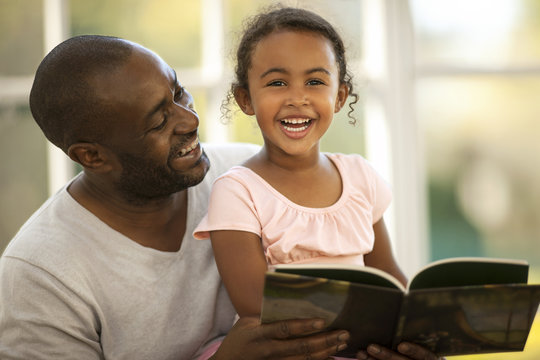Smiling father and daughter reading book at home