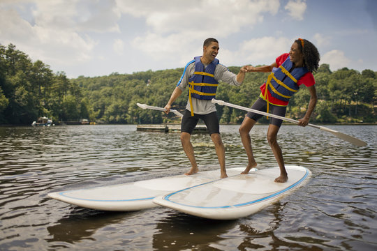 Happy young couple playfully paddle boarding on a lake.