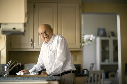 Smiling elderly man cleans up in the kitchen after lunch.