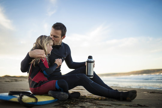 Father kissing daughter while sitting on beach