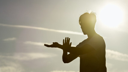 Silhouette male doing tai chi with the sun shining behind him - 153998841