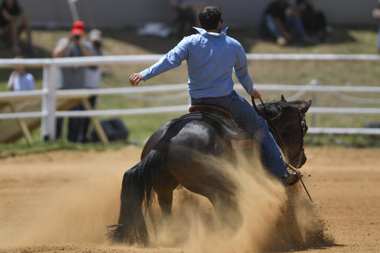 The rear view of a rider in cowboy chaps and boots sliding the horse in the sand