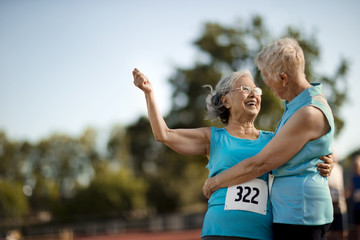 Two happy senior women embracing after competing in an athletic event.
