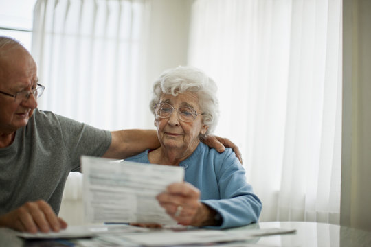 Anxious elderly couple try to comfort each other as they are worried about a bill that they have received.