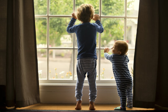 Young brothers looking eagerly out a window.