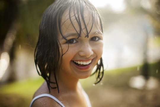 Portrait of a smiling young girl soaked from playing in the garden in the rain.