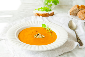 Vegan Creamy Delicious Pumkin Soup with fresh arugula and pamkin seeds and sliced bread on the white table. Selective focus.
