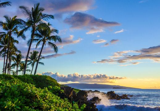 Beautiful tropical beach at sunset. Palm trees and lush local foliage.  Water splashing on lava rocks.  Tourist destination location at Maui, Hawaii - Powered by Adobe