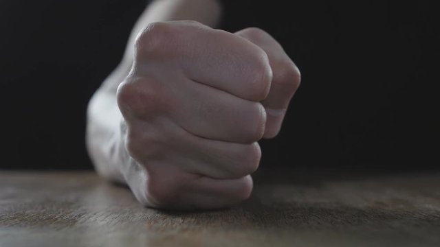 Fist of angry man beats on the table in slow motion