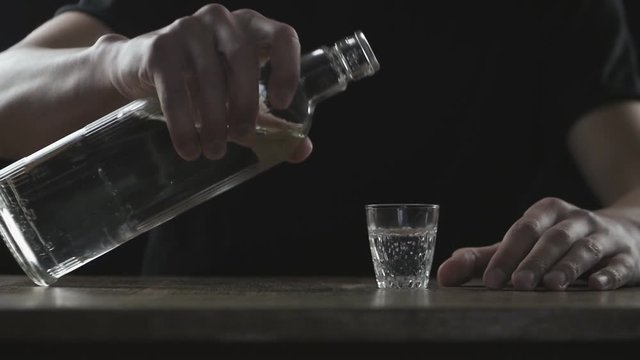 Concept of alcoholism. Man pours alcohol into a glass and drinks in a dark room in slow-motion