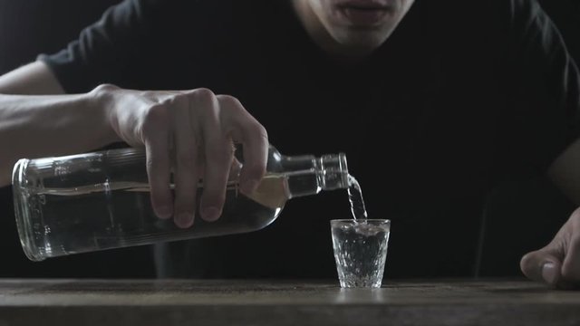 Concept of alcoholism. Man drinking vodka alone in a dark room in slow-motion