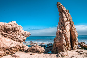 Fototapeta premium Large rocks on a rocky beach with a blue cloudy sky