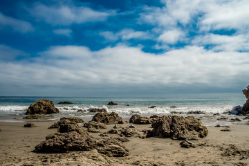 Fototapeta na wymiar Rocky beach with a blue cloudy sky