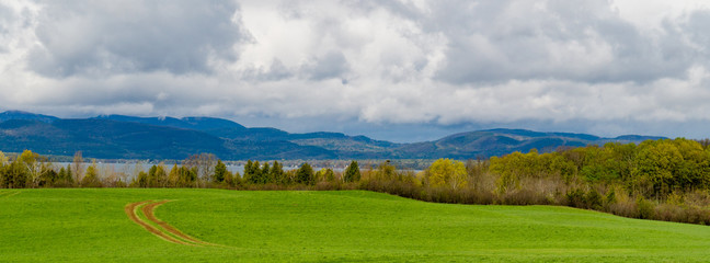 banner picture of farm meadow with tractor tracks curving across field  looking to Lake Champlain, Vermont , across to mountains in New York State
