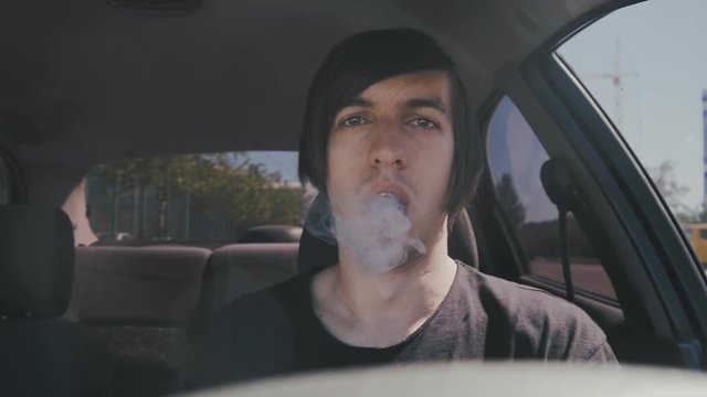 Man vaper makes smoke with electronic cigarette sitting in car in slow-motion