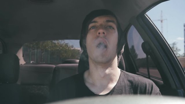 Man vaper makes smoke with electronic cigarette sitting in car in slowmotion.