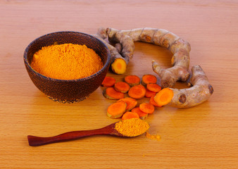 Turmeric powder in wooden spoon on wooden table.