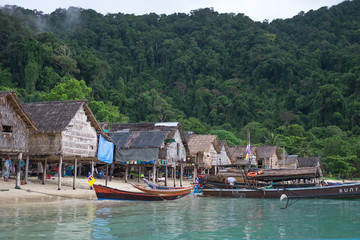 longtail boat parked on sea have old village and forest on mountain are background. this image for landscape,travel,culture and nature concept
