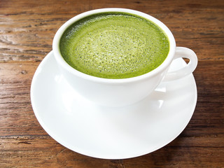Hot green tea matcha latte cup with white saucer on wood texture background.