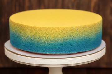 Blue and yellow cake on stand over wooden background