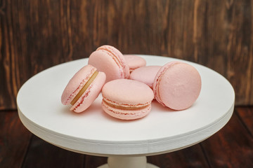 Pink macaroons on white stand on wooden background, homemade food
