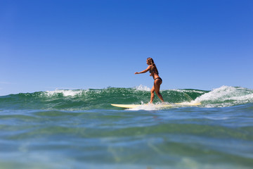 A healthy, tanned girl surfs over pristine clear water during summer in Australia.