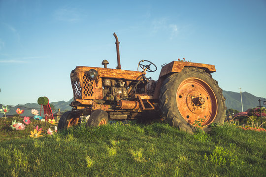 old Tractor parked on meadow against blue sky.